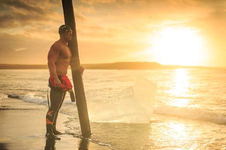 Ross Edgley stands with tree trunk on beach at sunset.