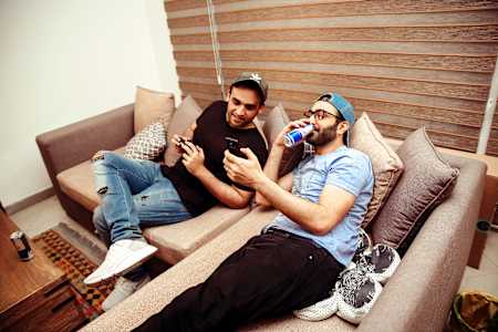 Studenci siedzący na kanapie, pijący Red Bulla i przeglądający najnowsze memy