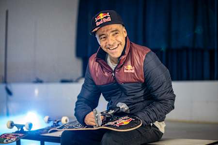 Sandro Dias lächelt mit seinem Skateboard in der Hand.