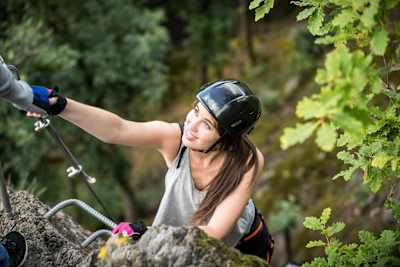 Woman gets a helping hand climbing a via ferrata.