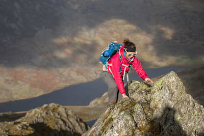 Woman scrambles above a tarn in Tryfan, Wales.
