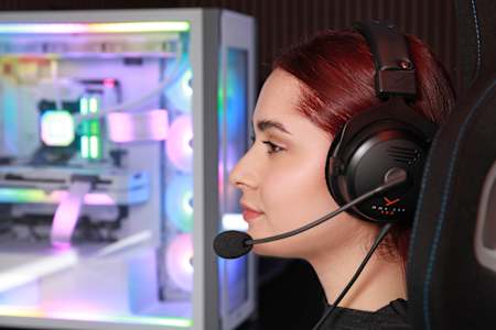 Bild zeigt eine junge Frau mit dem beyerdynamic MMX 330 Pro Gaming-Headset mit einem Gaming-PC im Hintergrund.