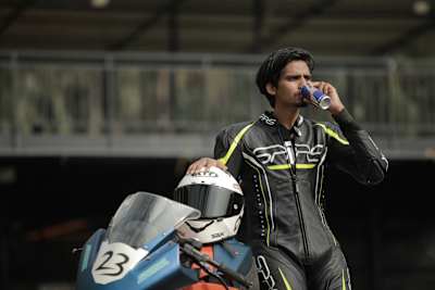 Bike racer Allwin Xavier stands with his race bike while drinking Red Bull
