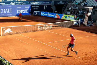 Toprak tenis kortundaki oyuncuların görüntüsü.