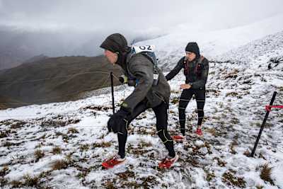 Adventure racers climb up mountain side in snowy conditions.