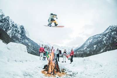 Nitro snowboarder airs over a burning campfire.