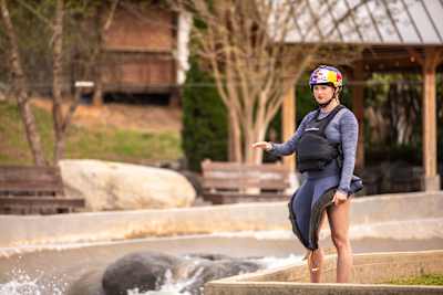 Evy Leibfarth standing next to whitewaters, in wetsuit and wearing a Red Bull helmet. 