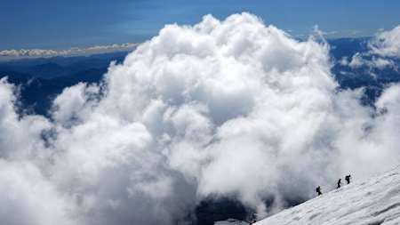 Hikers on snowy ascent pass clouds produced from Villarica volcano.
