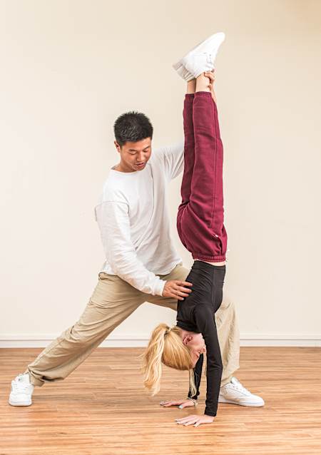 Chau-Lin, miembro de HE4DS, corrige la postura de una bailarina mientras esta hace el pino.