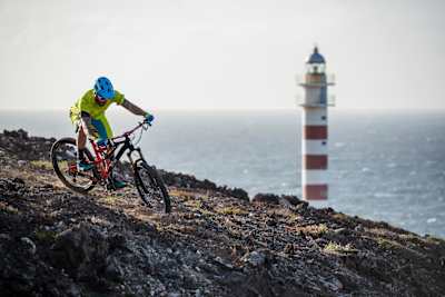 Ein Mountainbiker fährt an einem Leuchtturm auf den Klippen an der Küste von Gran Canaria vorbei.