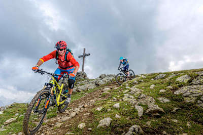 Zwei Mountainbiker passieren das Gipfelkreuz auf dem MTB-Trail Stoneman, Marchkinkele.