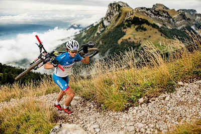Rider carrying a bike up a steep incline on his back.