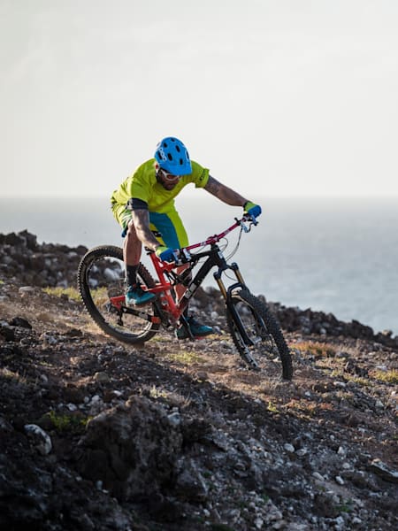 Ein Mountainbiker fährt an einem Leuchtturm auf den Klippen an der Küste von Gran Canaria vorbei.