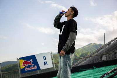 Tomomi Nishikubo beve una lattina di Red Bull su un trampolino di salto con gli sci a Hakuba, in Giappone, nel maggio 2026.