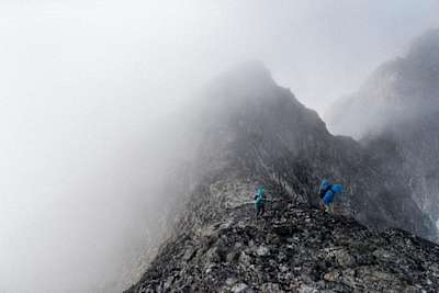 Hikers wearing Arc’teryx backpacks in mist on a mountain ridge.