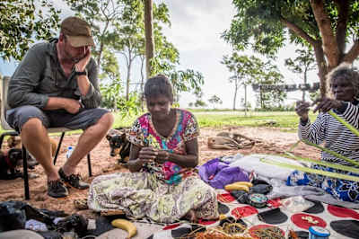 Turista observa mulheres aborígenes australianas a fazer artesanato.