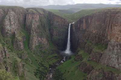 Grande cascata e falésias rodeadas por um vale verdejante.