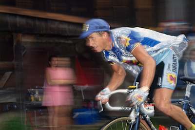 Greg Lemond rides his bike past a stall holder in an image blurred by speed.