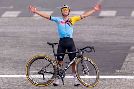 Belgian rider Remco Evenepoel stands beside his bike with arms raised. 