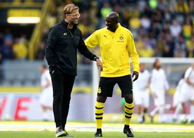 Jürgen Klopp als BVB-Trainer im Stadion auf dem Platz grinsend mit einem seiner Spieler.