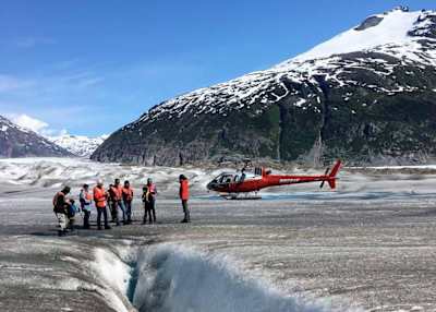 Group of people stood next to helicopter on glacier in Alaska.