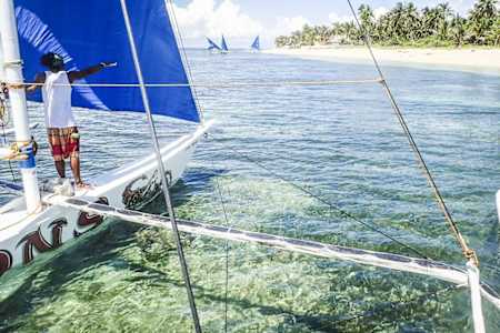 Sailor adjusts sail in exotic clear seas.