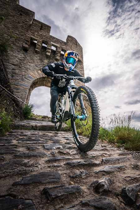 A close-up shot from the ground looking up, with the downhill bike rider racing past the camera, with a stone arch in the background at Castle Ride.