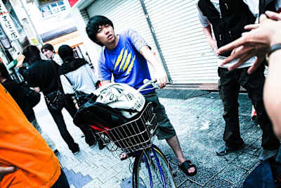 A young Hajime ‘Tokido’ Taniguchi sports a Madcatz shirt while straddling a bike in a street in Japan.