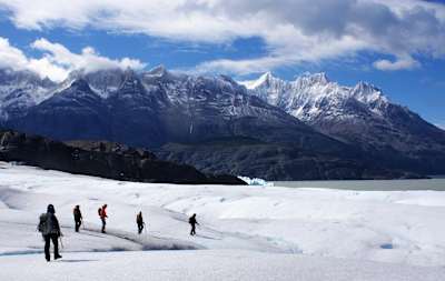 People walk across glacier towards lake in Chile.