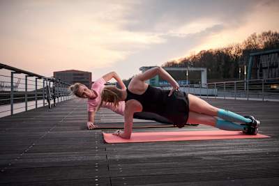 Women do side planks on a wooden jetty.
