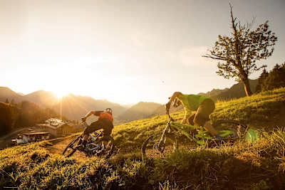 Mountain bikers come around a berm and head into the sunset.
