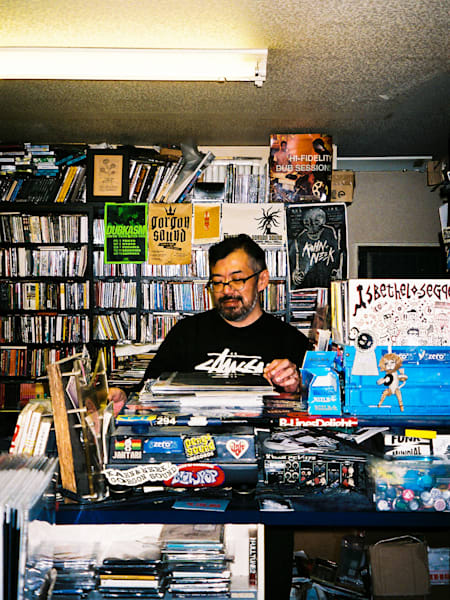 A photo of Naoki E-JIMA at the shop counter at his record store Disc Shop Zero.