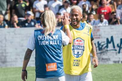 Neymar Jr. lächelt beim Red Bull Neymar Jr.'s Five und klatscht mit einer Mitspielerin ab.