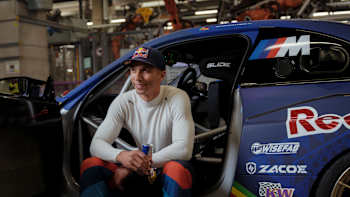 Drift ace Eli Hountondji from the Red Bull Driftbrothers poses for a portrait photo with a Red Bull can in his hand in front of his new drift car, the BMW M2 Drift Competition.