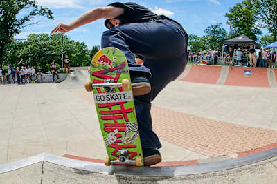 Deskorolkowiec robi trik na zielonej deskorolce z czerwonym napisem.