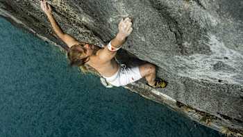 A climber attempts a rope-free deep water soloing climbing route above the sea, which is his safety net should he fall