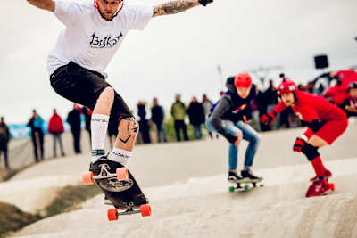 Chłopak w białej koszulce jedzie z podniesionymi przednimi kółkami do góry.