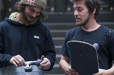 Dwóch deskorolkowców ogląda deskorolkowe trucki, które osoba po lewej trzyma w rękach