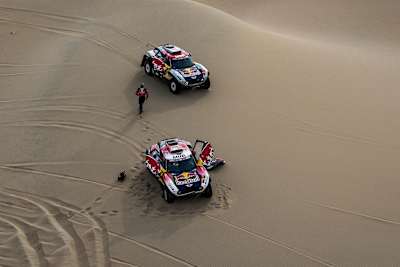 A photo of Stephane Peterhansel, Cyril Despres and Jean-Paul Cottret helping X-Raid Mini JCW team-mate David Castera in the dunes during the Dakar Rally 2019.