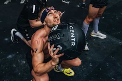 Un athlète réalise l'épreuve des Wall Balls lors d'une compétition HYROX, enchaînant les squats et les lancers d'un ballon lesté.