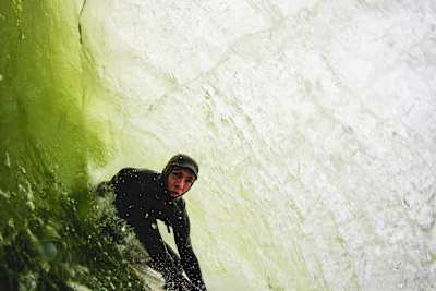 Irish surfer Conor Maguire rides a wave that breaks onto dry rock.