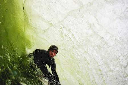 Irish surfer Conor Maguire rides a wave that breaks onto dry rock.