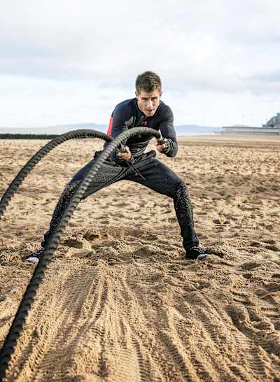 Explorer Ash Dykes using battle ropes to train his core and upper body on a beach in North Wales.