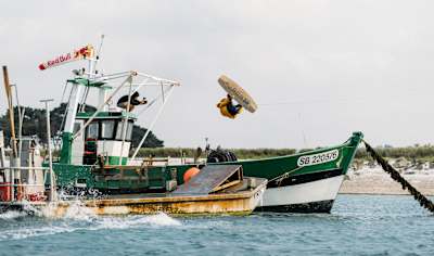 Jules Charraud réalise une figure en wakeboard sur un bateau en Bretagne.