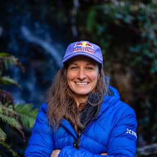 Nadine Wallner, dressed in a Red Bull cap and blue outdoor gear, stands in scenic Ticino, Switzerland during an exciting 2025 adventure, embodying Red Bull's spirit of exploration.