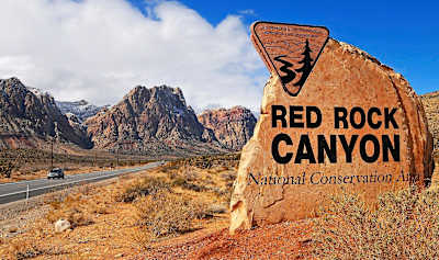 Red Rock Canyon National Conservation area sign with rocky outcrops and road behind.