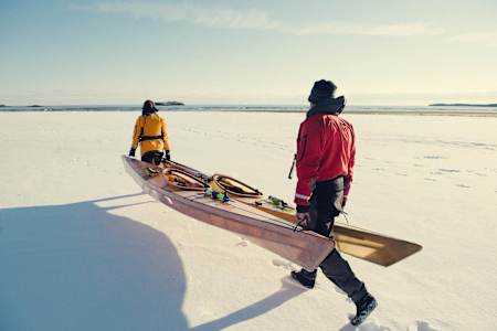 A traditional skin-on-frame kayak being carried across pack ice in the Arctic Circle
