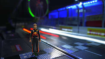 A screen-grab image of Daniel Ricciardo standing on a slot-car recreation of the Marina Bay Street Circuit in Singapore.