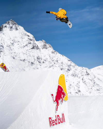 In 2024, Mark McMorris performs an aerial trick at Red Bull's event in Saas-Fee, showcasing his snowboarding skills against a stunning mountain backdrop.