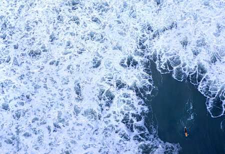 A surfer chasing the whitewater during large storm surf at Swamis Beach.